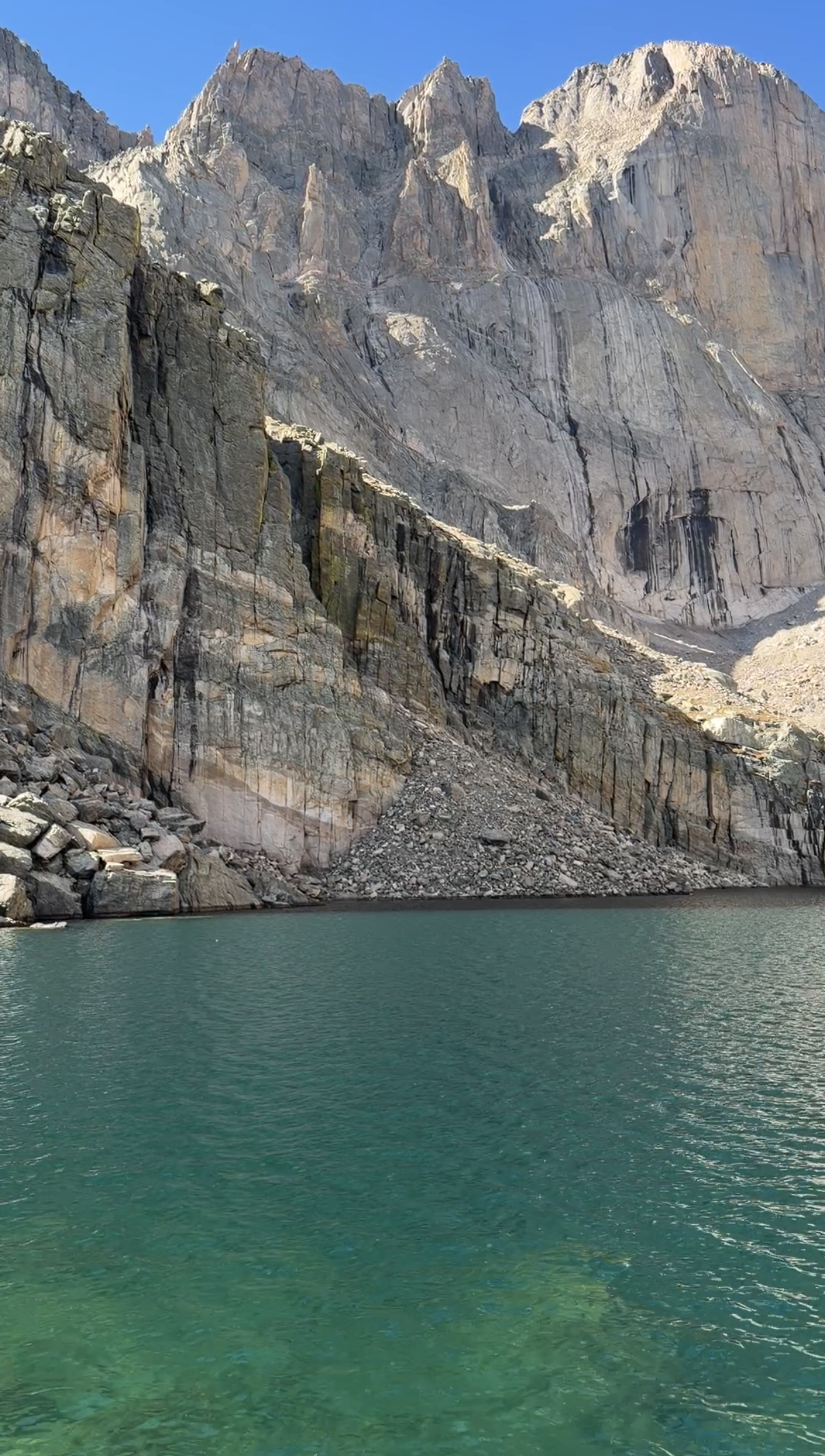 Turquoise water at Chasm Lake beneath towering granite cliffs and a clear blue sky